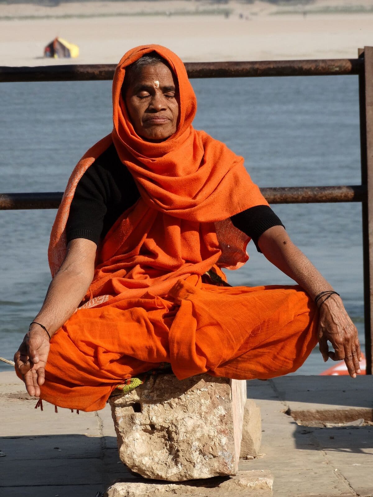 A practitioner in ochre robes seated in meditation beside the water